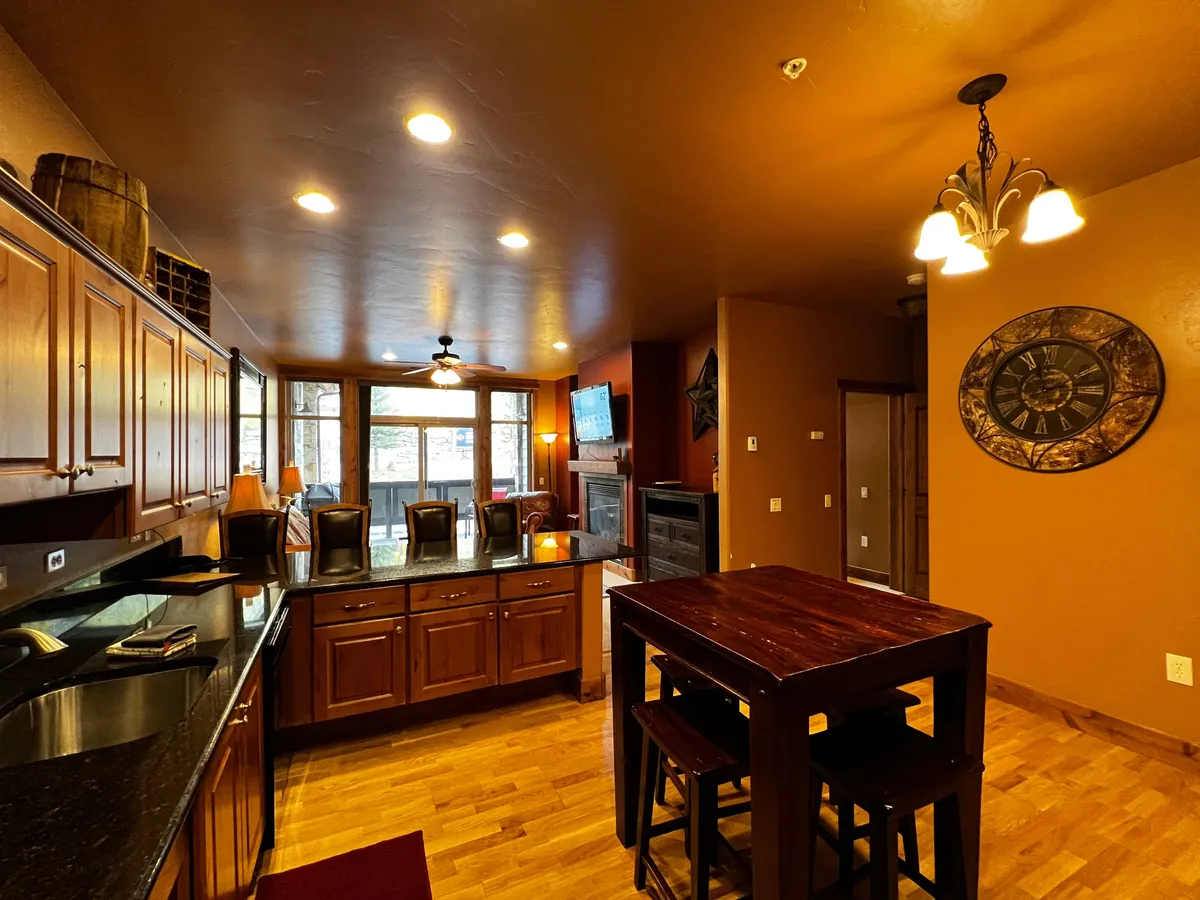 A spacious, open interior merges the kitchen and dining spaces, featuring a kitchen island, wooden cabinets, a welcoming dining area with chairs, a fireplace, and a television nearby. The layout encourages socializing and togetherness.