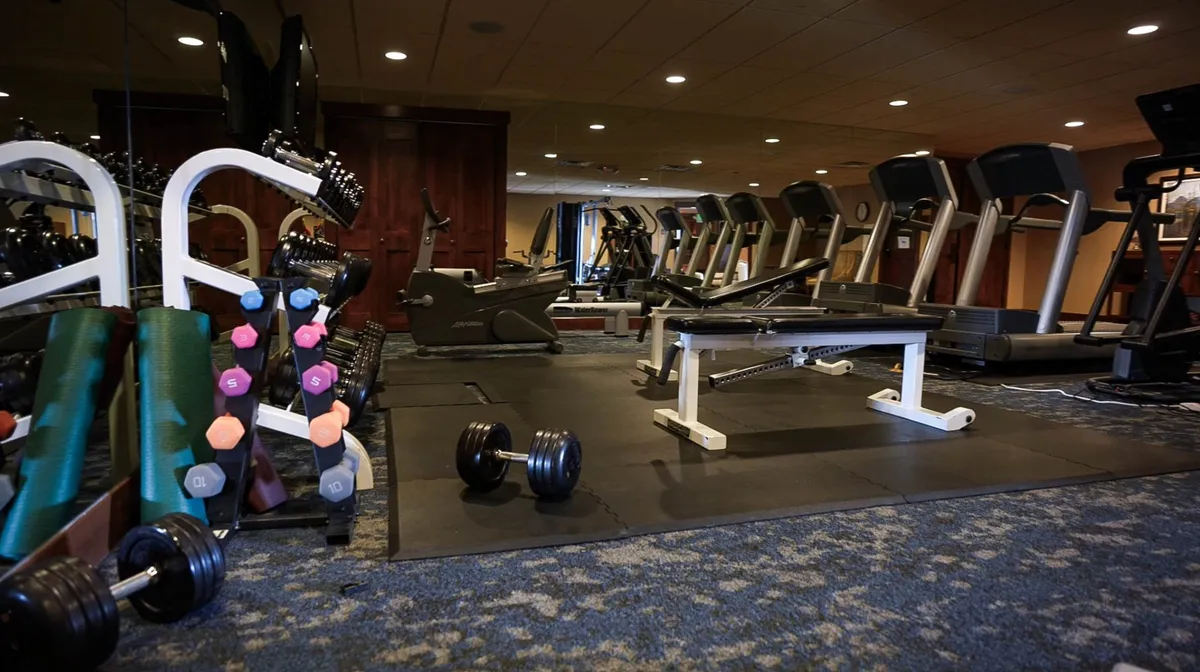 A bright, modern fitness room with treadmills, dumbbells, and a weight bench, ready for guests to pursue workouts and wellness routines after outdoor adventure.