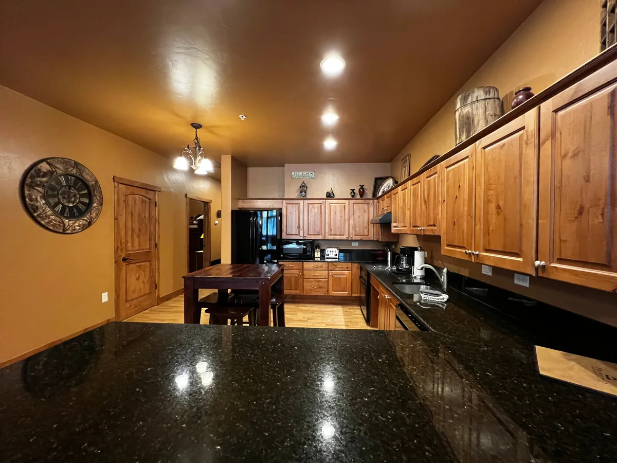 A warm, cozy kitchen interior featuring granite countertops, wooden cabinets, and black appliances. The kitchen is inviting and ideal for preparing group meals, entertaining friends, and gathering before or after local outings.