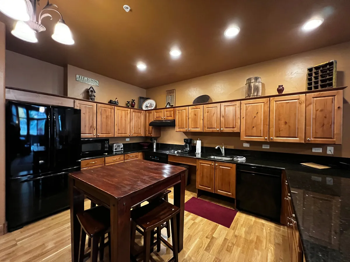 A cozy kitchen scene highlighting a kitchen island, black appliances, wooden cabinets, and granite countertops. The space feels intimate and practical, designed for everything from baking to casual family meals.