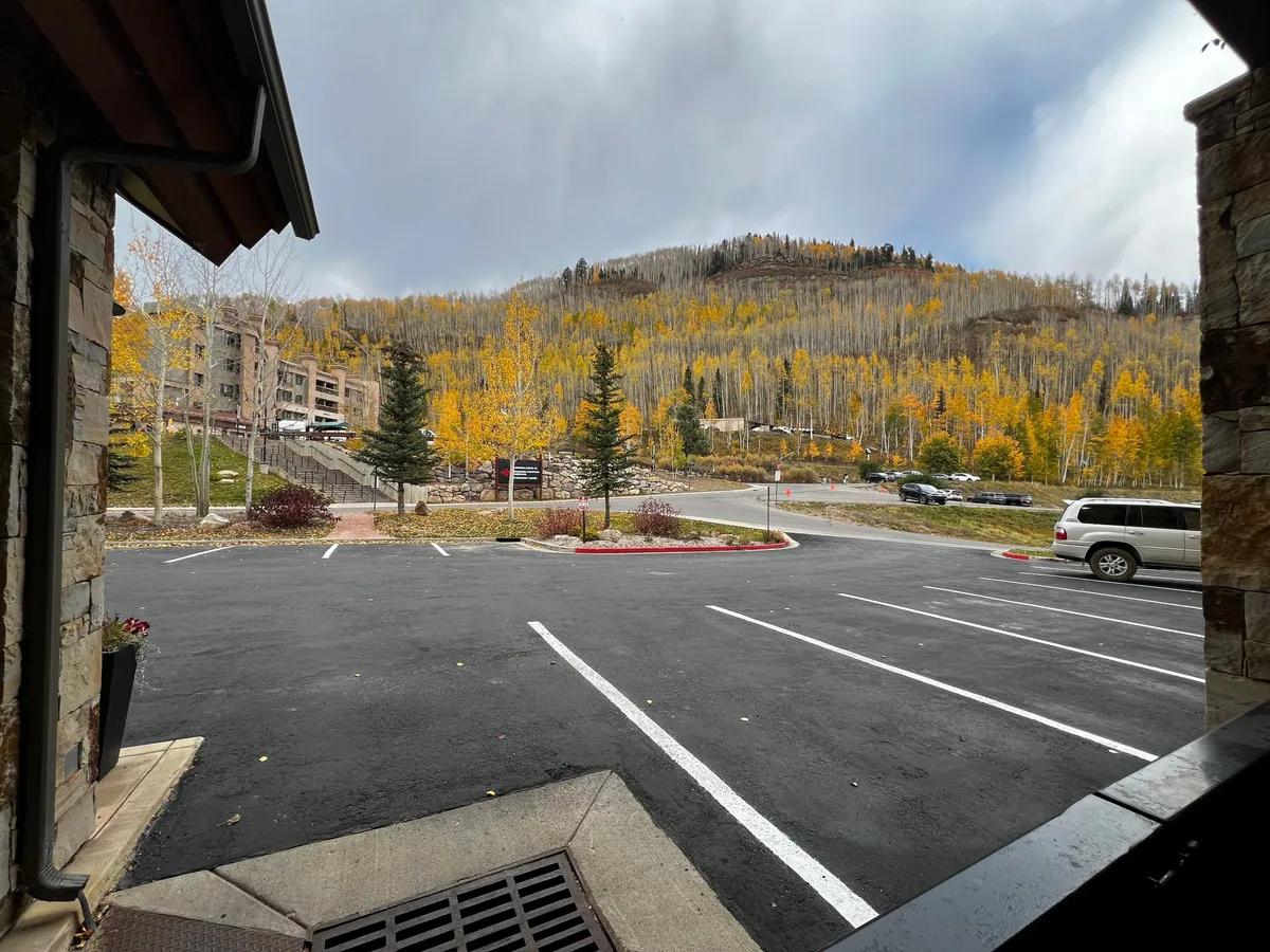 A scenic exterior view of Peregrine Point during autumn, showing the building nestled among colorful trees with mountains in the background. The parking lot in front suggests easy access for day trips, while the landscape highlights the property's mountain setting.