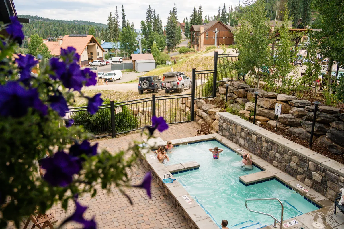A heated outdoor hot tub set among lush greenery with a mountain view and residential resort buildings in the background. The space feels inviting and relaxing, perfect for families to unwind together after an active day.