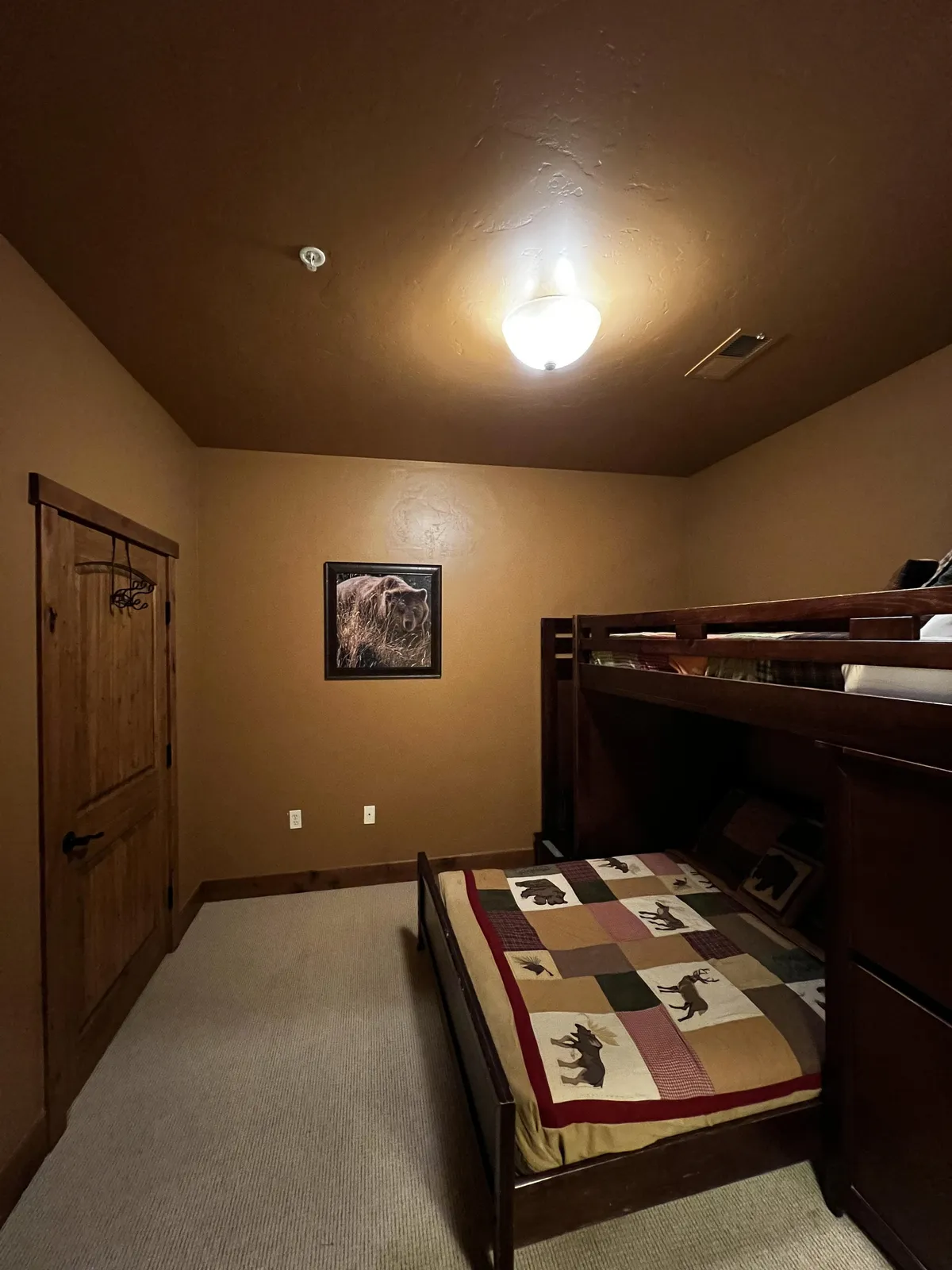 A cheerful guest bedroom with a distinctive bunk bed (double below and single above), complemented by playful bear artwork and a patterned bedspread. Natural light streams in, evoking a sense of warmth and family-friendly comfort.