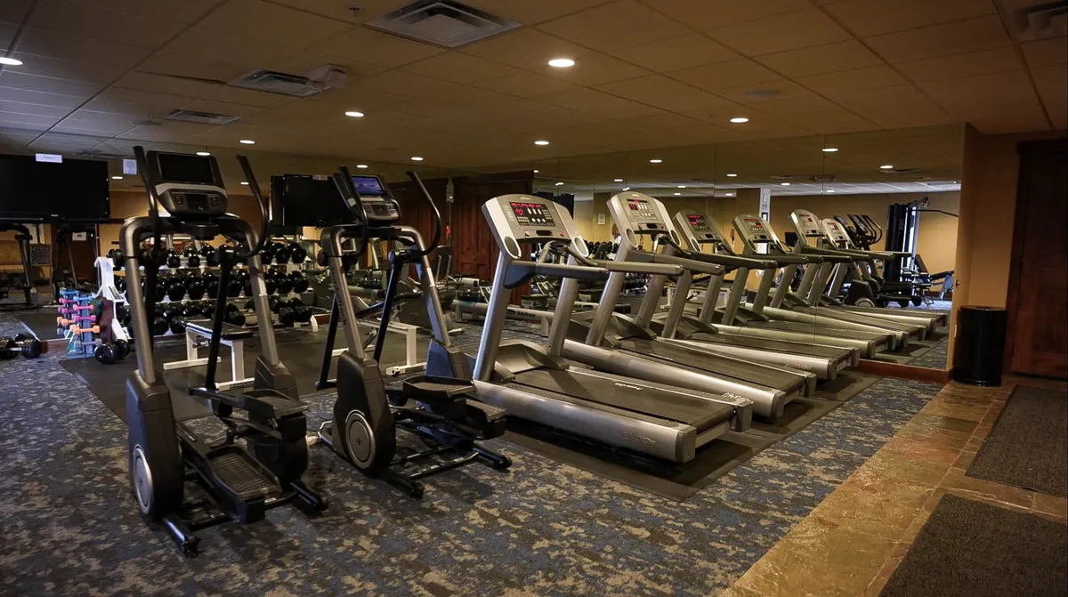 A modern, well-lit fitness room equipped with treadmills, ellipticals, free weights, and a mirrored wall. The clean and motivational space encourages guests to maintain their fitness routines during their stay.