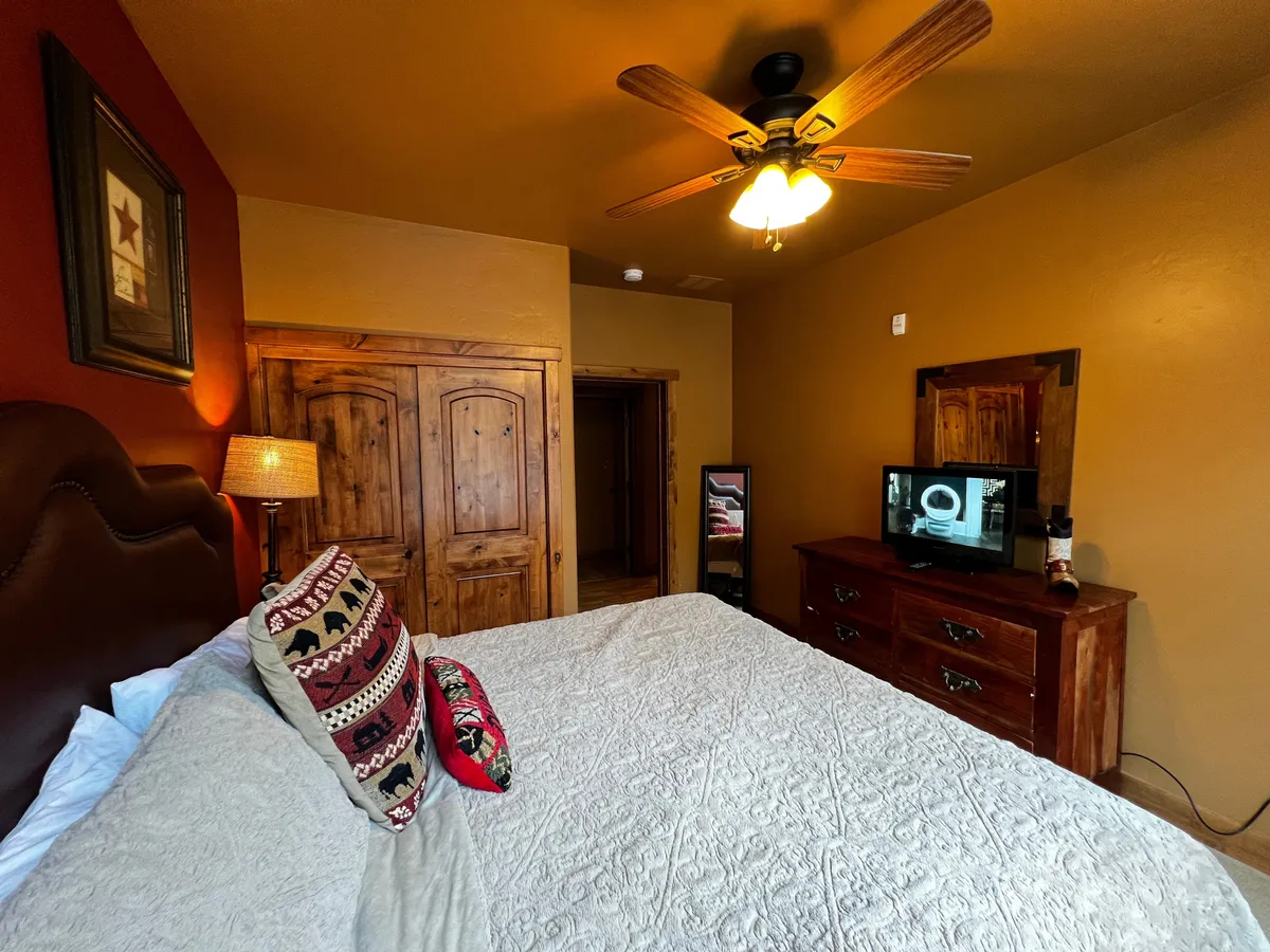 A warm, inviting master bedroom featuring a king bed dressed with decorative pillows, a wooden dresser, and a ceiling fan overhead. The space is bathed in soft light, creating a perfect retreat for relaxation after an active day.