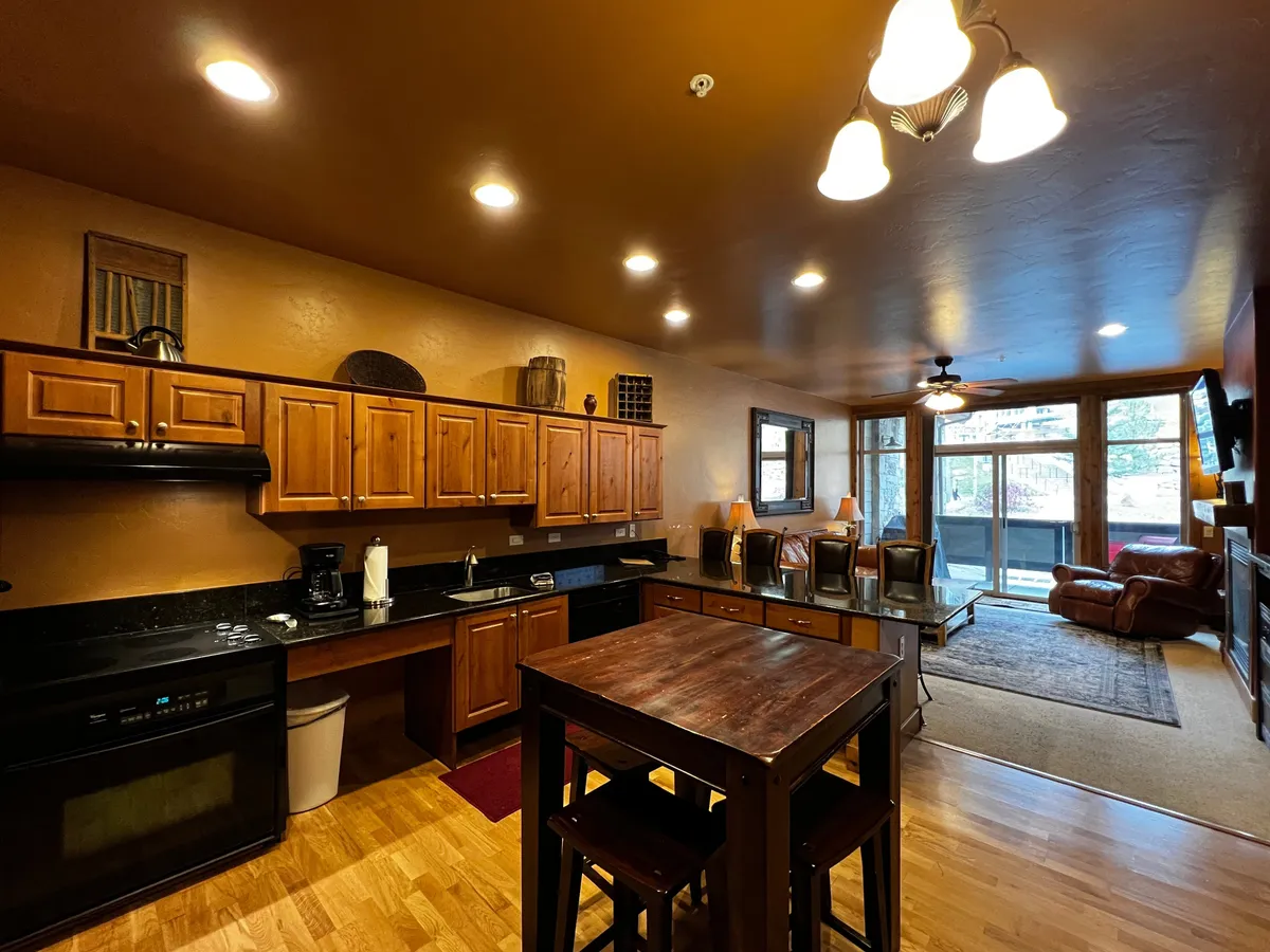 This image showcases a spacious kitchen with wooden cabinets, a black countertop, a kitchen island, and large windows that allow natural light to flood the space. The comfortable seating area nearby hints at opportunities for gathering and entertaining while cooking.